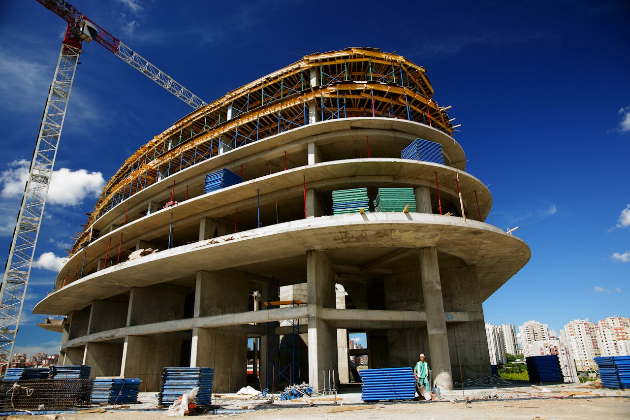 about-01 Low angle view of a circular building under construction with a crane, clear blue sky.