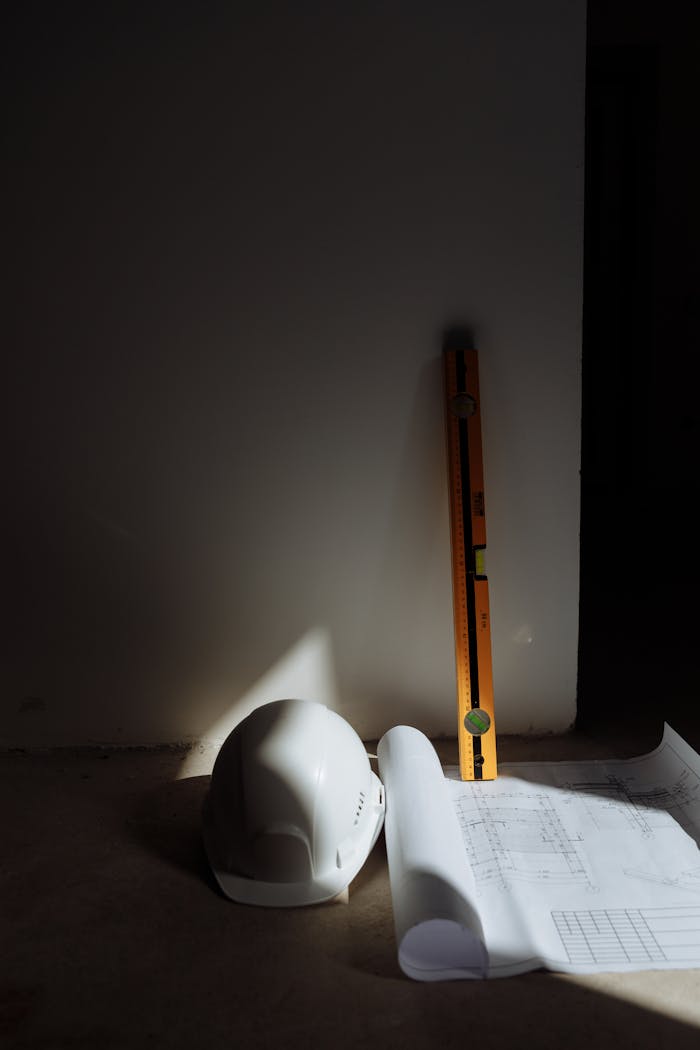 why-choose-us-02 A hard hat, level, and blueprints in a construction setting, highlighting precision.